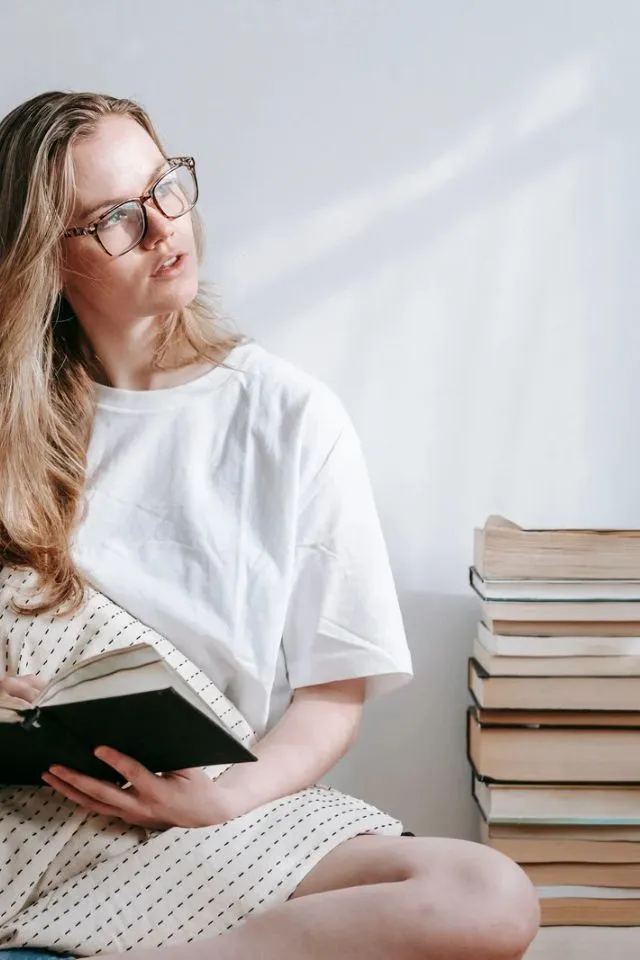 Speed Reading - Frau mit Brille, Buch in der Hand, Stapel Bücher daneben